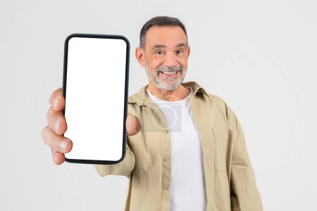 Un aîné debout tenant un téléphone intelligent dans sa main, regardant l'écran. Le visage des hommes est concentré pendant qu'il interagit avec l'appareil, éventuellement en envoyant des SMS, en naviguant ou en prenant un appel.