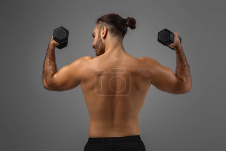 A man with a ponytail is shown holding two dumbbells in his hands. He appears focused and ready to engage in a workout or exercise routine, back view
