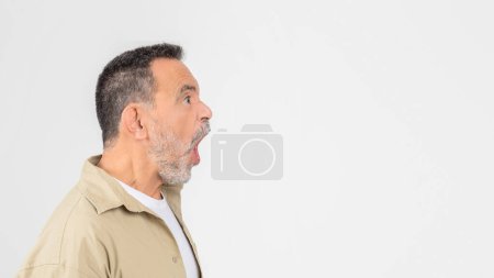 Ein älterer Mann im hellen Hemd verzerrt seinen Gesichtsausdruck, zeigt einen humorvollen oder übertriebenen Blick und schreit in Richtung Kopierraum auf Weiß.