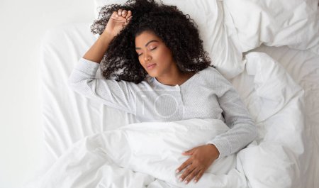 Foto de Una mujer hispana está acostada cómodamente en una cama cubierta con sábanas blancas crujientes. Ella parece relajada y está rodeada por un ambiente sereno. - Imagen libre de derechos
