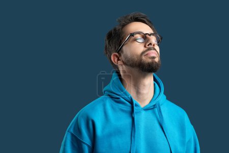A man wearing glasses is looking upwards towards the sky, his expression curious and thoughtful. He is standing over blue background