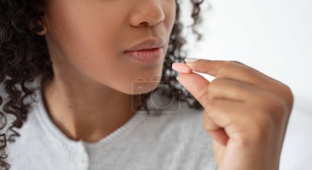 Foto de Una vista de cerca captura un momento en el que una mujer joven con el pelo rizado está a punto de consumir una pequeña píldora, destacando la importancia de la salud y la adhesión diaria a la medicación, recortada - Imagen libre de derechos