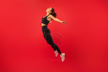 A woman in black sports bra and leggings is mid-air, jumping energetically. She is captured in a moment of athleticism and motion, showcasing her strength and agility.