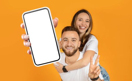 Joyeux jeune couple debout ensemble, les deux tenant un téléphone portable vers la caméra. Ils regardent l'écran du téléphone, peut-être en prenant un selfie ou un appel vidéo.