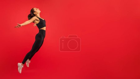 A woman is captured mid-jump against a vibrant red background. Her body is suspended in the air, exuding a sense of energy and motion, copy space