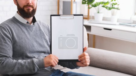 Photo for Confident psychotherapist showing white blank clipboard at camera, sitting in office, free space for announcement - Royalty Free Image