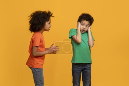 Niña afroamericana parece estar hablando animadamente con un niño, que se cubre los oídos con las manos, lo que posiblemente indica que no está interesado en escuchar lo que tiene que decir.