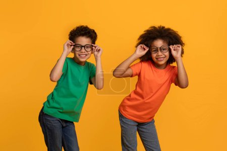 Téléchargez les photos : Deux enfants afro-américains, tous deux portant des lunettes, prennent une pose pour un appareil photo. Ils semblent joyeux et excités, regardant directement l'objectif avec de grands sourires - en image libre de droit