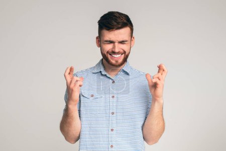 Photo for Young guy with closed eyes hopes for fortune and good luck with crossed fingers on studio background, panorama - Royalty Free Image