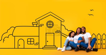 Excited black family of three father mother and teen daughter sitting on floor and looking at illustrated house of their dreams over yellow wall background