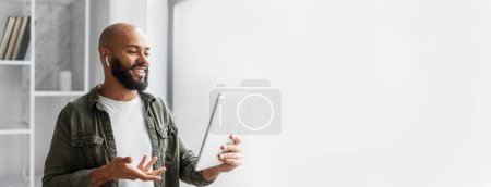 Ein afrikanisch-amerikanischer Mann mit Kopfhörer spricht begeistert in ein Tablet, was auf einen Videoanruf mit Kopierraum und Webbanner-Layout hindeutet.