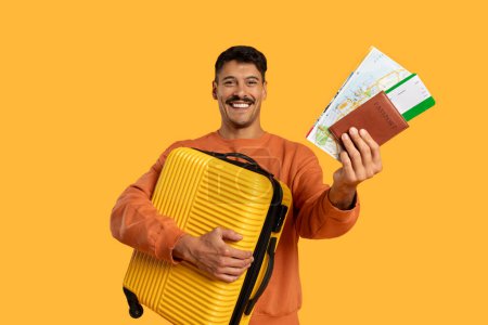 Téléchargez les photos : Un homme debout tenant une valise jaune dans une main et un passeport dans l'autre. Il semble se préparer pour le voyage, avec ses affaires prêtes. - en image libre de droit