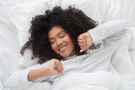 Eine Frau liegt mit geschlossenen Augen in einem Bett und ruht friedlich in einem Schlafzimmerambiente, Blick von oben