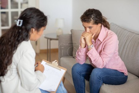 Stressé jeune femme souffrant d'anxiété, assis sur le canapé à la clinique, toucher son visage, avoir une séance thérapeutique avec le psychologue