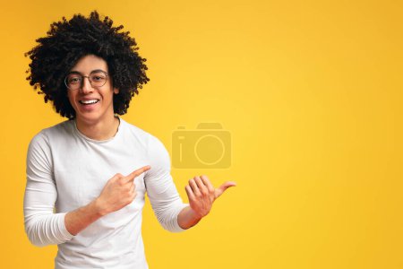 Foto de Chico negro lindo apuntando hacia el espacio vacío, mostrando una nueva oferta sobre fondo naranja - Imagen libre de derechos