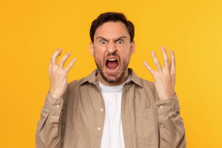 Photo for A man with dark hair is passionately expressing his frustration, his hands raised in the air, his mouth wide open in a shout, with a vivid yellow backdrop emphasizing his strong emotion. - Royalty Free Image