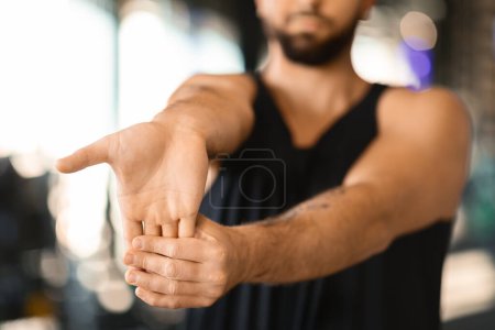 Gestutzter junger Mann mit Bart wird in der Mitte der Bewegung gezeigt, während er sein Handgelenk in einem Trainingsbereich streckt, möglicherweise als Teil einer Aufwärm- oder Abklingroutine