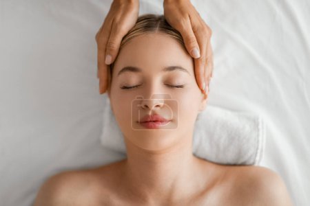 Photo for A serene woman with closed eyes is lying down, experiencing the calming touch of head massage at spa, conveys sense of tranquility and wellbeing as the masseuses hands gently press on her temples - Royalty Free Image