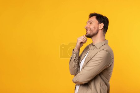 Téléchargez les photos : Un homme se tient devant un fond jaune vif. Il semble poser ou observer quelque chose, regarder l'espace de copie - en image libre de droit