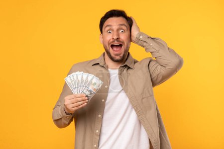Photo for A man humorously holds a stack of money in one hand, while contorting his face into a silly expression. His eyes widen and mouth stretches into a big grin, conveying joy and playfulness. - Royalty Free Image