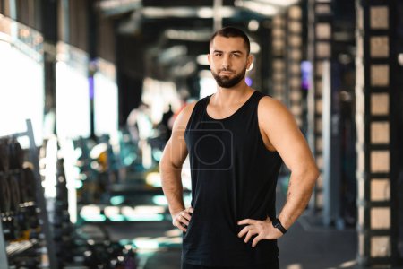 Photo for A man standing confidently in a gym, with his hands resting on his hips. He appears focused and determined, ready for his workout session. - Royalty Free Image