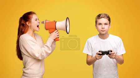 Mother shouting through megaphone at boy playing with joystick, orange studio background