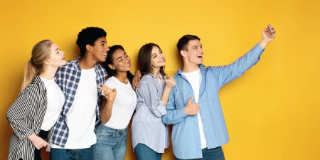 Foto de Un grupo diverso de cinco adolescentes multiétnicos se reúne estrechamente, posando para un selfie. Uno de ellos sostiene un teléfono inteligente con un brazo extendido - Imagen libre de derechos