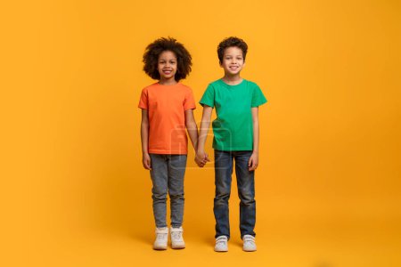 Téléchargez les photos : Deux enfants afro-américains se tiennent côte à côte, regardant droit devant. Ils portent tous les deux des vêtements décontractés et semblent détendus dans l'autre compagnie. - en image libre de droit