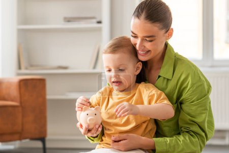 A woman holds a young child who clutches a vivid pink piggy bank in their hands. Mother and son figures appear engaged with the object, showcasing a lesson in financial responsibility.