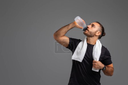A man is shown taking a drink from a plastic water bottle. He is holding the bottle with one hand and tilting it towards his mouth to hydrate himself, copy space