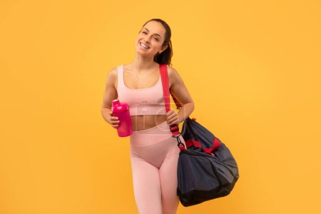 A woman dressed in a pink sports bra and leggings is holding a gym bag. She appears to be ready for a workout or heading to the gym.