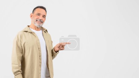 Un hombre mayor con una camisa bronceada está apuntando a un objeto o dirección, indicando algo de interés o importancia, panorama con espacio para copiar