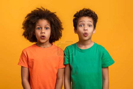 Afroamerikanische Jungen und Mädchen stehen Seite an Seite mit weit aufgerissenen Mündern in einem Blick der Überraschung vor einem leuchtend gelben Hintergrund.