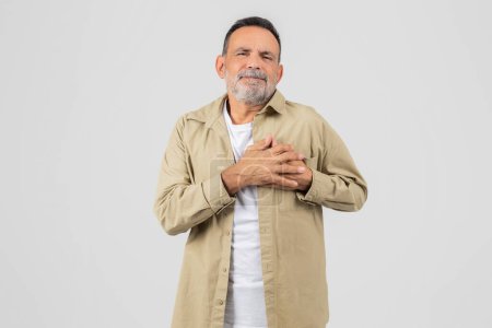 Photo for A senior man is standing upright with his hands neatly folded in front of his chest, experiencing heart attack on white background - Royalty Free Image