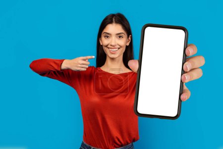 Téléchargez les photos : Une femme portant une chemise rouge tient un téléphone portable dans sa main, se concentrant intensément sur l'écran. Elle apparaît absorbée par l'appareil, peut-être en envoyant des textos ou en faisant défiler les médias sociaux. - en image libre de droit