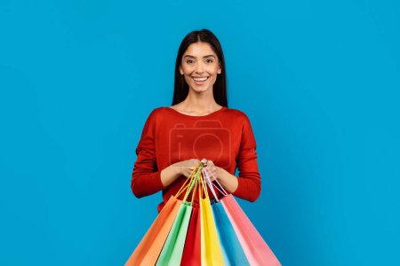 Una mujer está de pie mientras sostiene un montón de bolsas de compras vibrantes en varios colores. Ella parece llevarlos con facilidad, mostrando su juerga de compras.