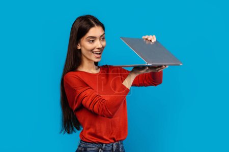 Téléchargez les photos : Une femme portant une chemise rouge tient un ordinateur portable dans ses mains. Elle semble se concentrer sur l'écran, peut-être travailler ou naviguer sur Internet - en image libre de droit