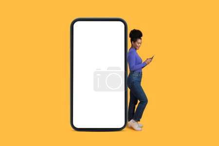 Téléchargez les photos : Femme hispanique debout à côté d'un téléphone avec un écran blanc, le regardant attentivement. Le téléphone est tenu dans sa main, sans notifications ou messages visibles à l'écran - en image libre de droit