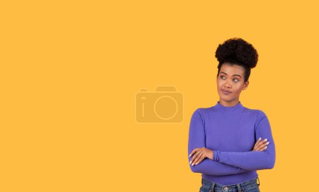 Téléchargez les photos : Femme hispanique se tient avec ses bras croisés devant un fond jaune vif. Elle semble confiante et affirmée dans sa posture, regardant l'espace de copie - en image libre de droit