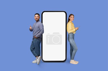 Téléchargez les photos : Un homme et une femme debout avec une maquette d'écran de smartphone vierge sur bleu, espace de copie de maquette pour la publicité d'application mobile - en image libre de droit