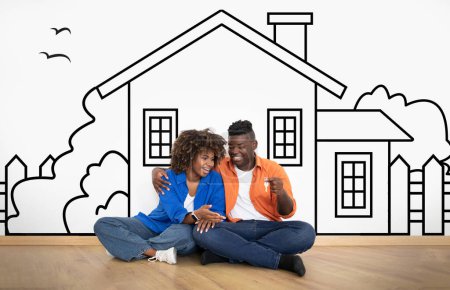 Photo for Cheerful young African American couple sitting by white wall with a house outline, dreaming of a home, holding key. Real estate, mortgage concept - Royalty Free Image