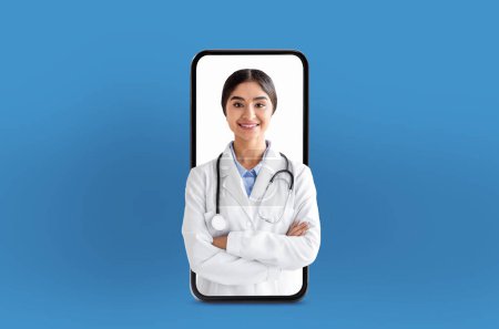 Médico joven indio proporciona servicios de salud digital, visto dentro de la pantalla en blanco de un teléfono inteligente, en comparación con un fondo médico simple.