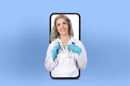 Una doctora madura aparece dentro de un teléfono inteligente para consultas en línea, ejemplificando la medicina moderna en un ambiente de clínica elegante.