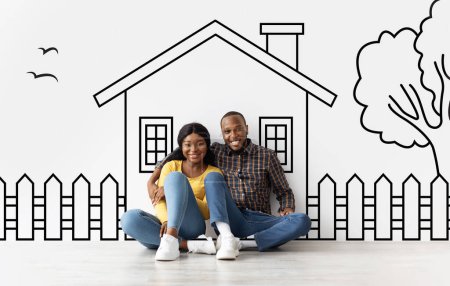 Photo for Loving African American young family husband and wife sitting over drawn on white wall house, embracing and smiling. Real estate, mortgage concept - Royalty Free Image