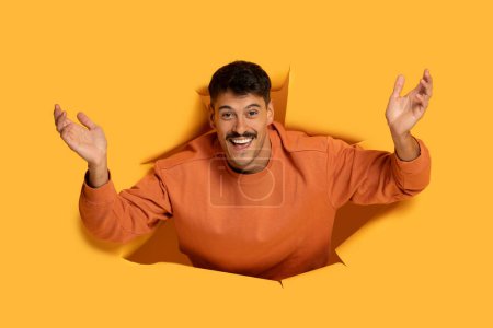 A cheerful man is bursting through an orange colored paper background, raising his hands in a playful and exuberant manner. His broad smile and dynamic pose convey a sense of fun and excitement