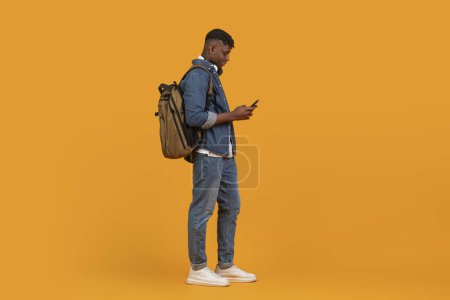 Afro-americano proyecta un ambiente multiétnico mientras revisa casualmente su teléfono, aislado sobre fondo naranja