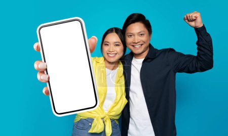 Joyeux jeune couple asiatique debout ensemble tenant téléphone cellulaire devant eux. Ils semblent tous deux engagés avec l'appareil, peut-être en prenant un selfie ou un chat vidéo. Le fond est indistinct.