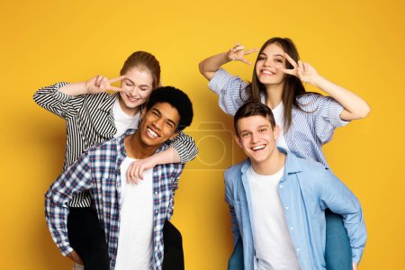 Photo for A cheerful group of four young friends is playfully posing together, with two making peace signs near their eyes and all sporting genuine, joyful smiles. - Royalty Free Image