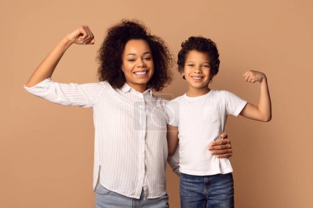 A smiling African American woman and a young boy are flexing their muscles together, showcasing a bond of strength and confidence.