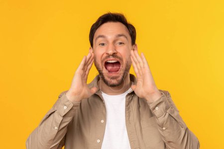 A man with a stubble beard and light brown hair is cupping his hands around his mouth as if shouting or making an announcement, yellow background